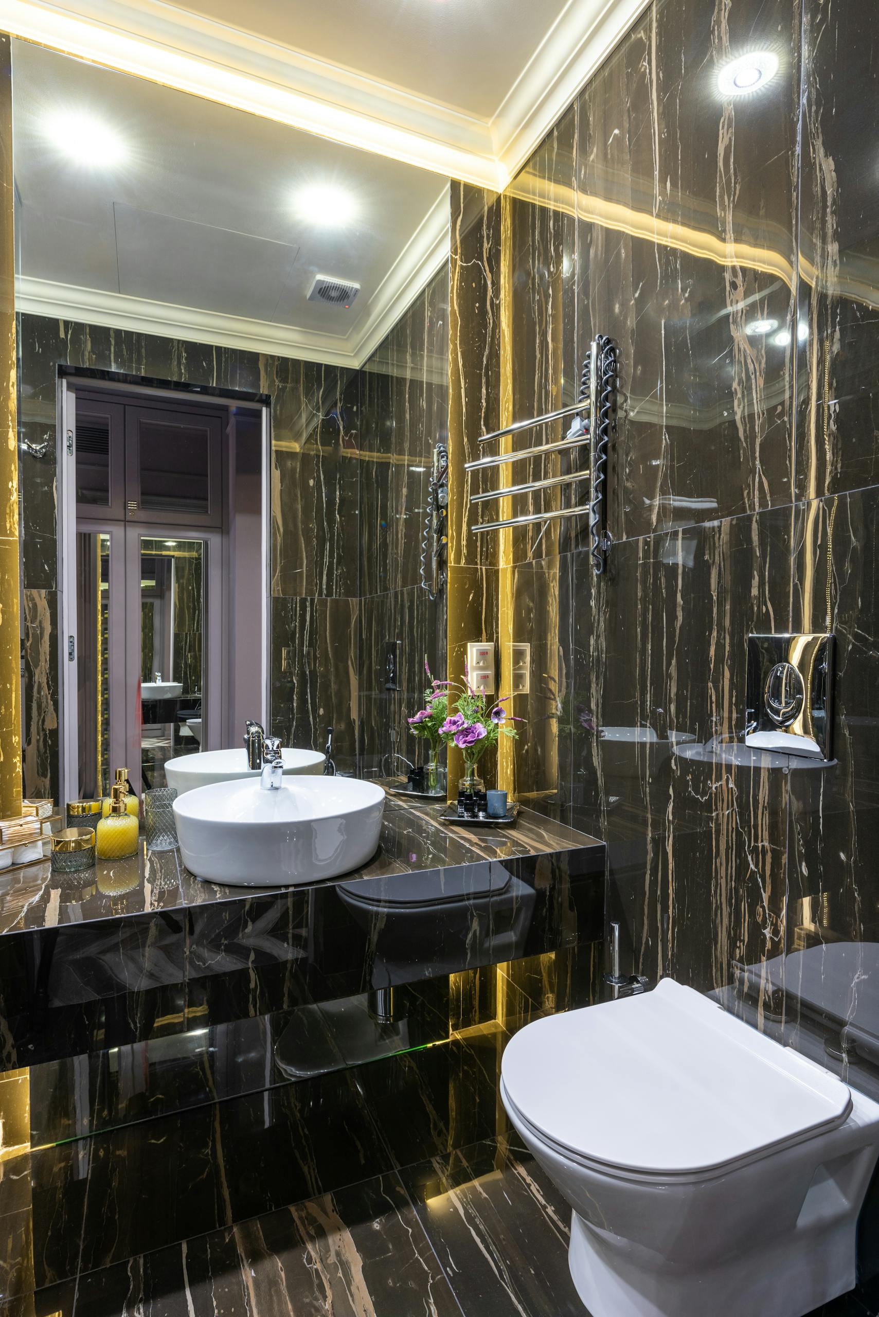 Contemporary bathroom with toilet bowl and washbasin reflecting in mirror under glowing lights in house